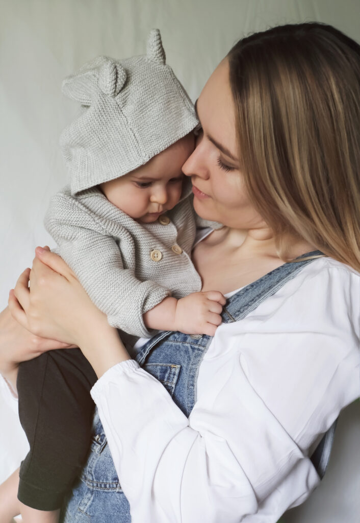 Young tender happy mother hugging her newborn baby smiling sitting on bed in morning.